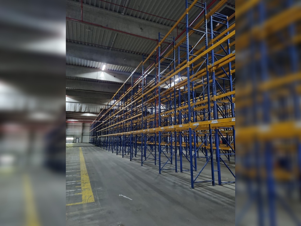 Jungheinrich Delta Palettenregal gebraucht in Lagerhalle, perspektivische Seitenansicht, Rahmen blau, Traversen gelb.